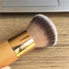 A golden bamboo airbrush foundation and bronzer brush with soft pink bristles resting on a wooden surface.