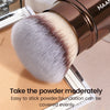 A close-up of a brown makeup brush with a fluffy, gradient pink and brown synthetic hair, shown next to a palette.