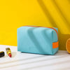 A light blue makeup bag with an orange color block accent resting on a white surface against a yellow wall.