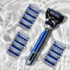 A stainless steel manual shaver with multiple blue shaving foils is displayed on a light surface.