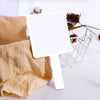 Miroir de maquillage portable blanc avec poignée, à côté d'une serviette beige sur une surface blanche.
