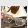 Une paire de lunettes de lecture carrées rétro transparentes avec une teinte ambrée posée sur une surface blanche.