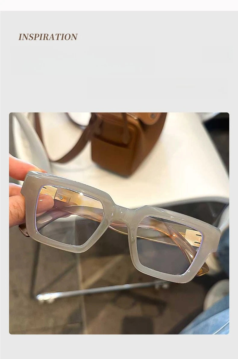 Une paire de lunettes de lecture carrées rétro transparentes avec une teinte ambrée posée sur une surface blanche.