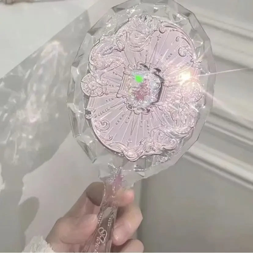 A hand holds a clear, ornate makeup mirror with a sparkling light emanating from the center.