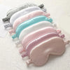A display of five layered silk sleep eye masks in pastel shades including gray, pink, and blue.