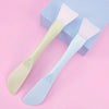 A light yellow silicone facial mask brush with a pink head is shown next to a blue box.