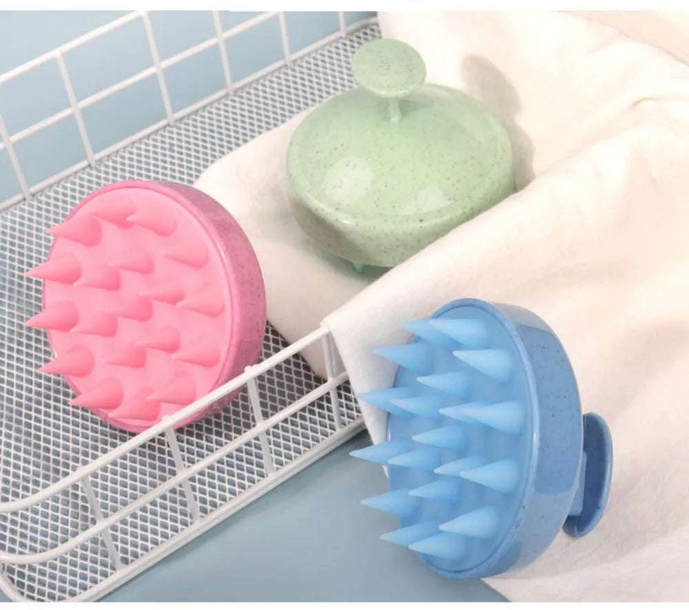 A pink silicone scalp massage brush and a blue silicone body brush are displayed on a white towel within a wire rack.