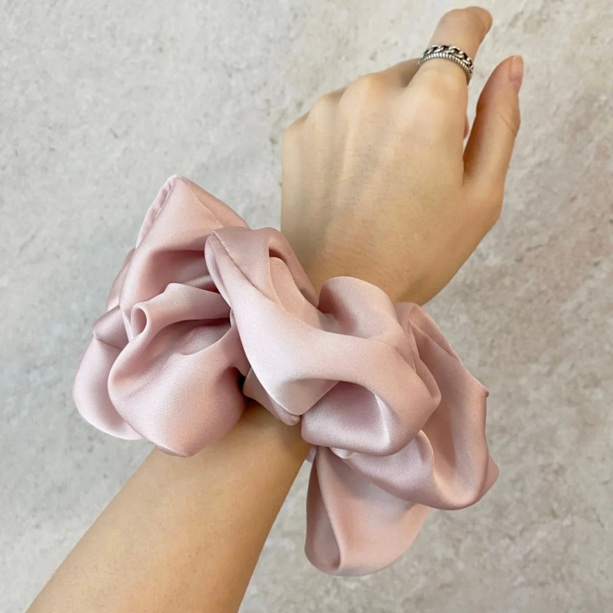Une main porte un élastique pour cheveux en mousseline de satin rose noué en nœud sur le poignet.