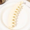 A white banana hair clip is shown on a white plate, next to a jar.