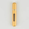 A tall, cylindrical gold-colored portable refillable perfume bottle with a silver band and a glass insert.