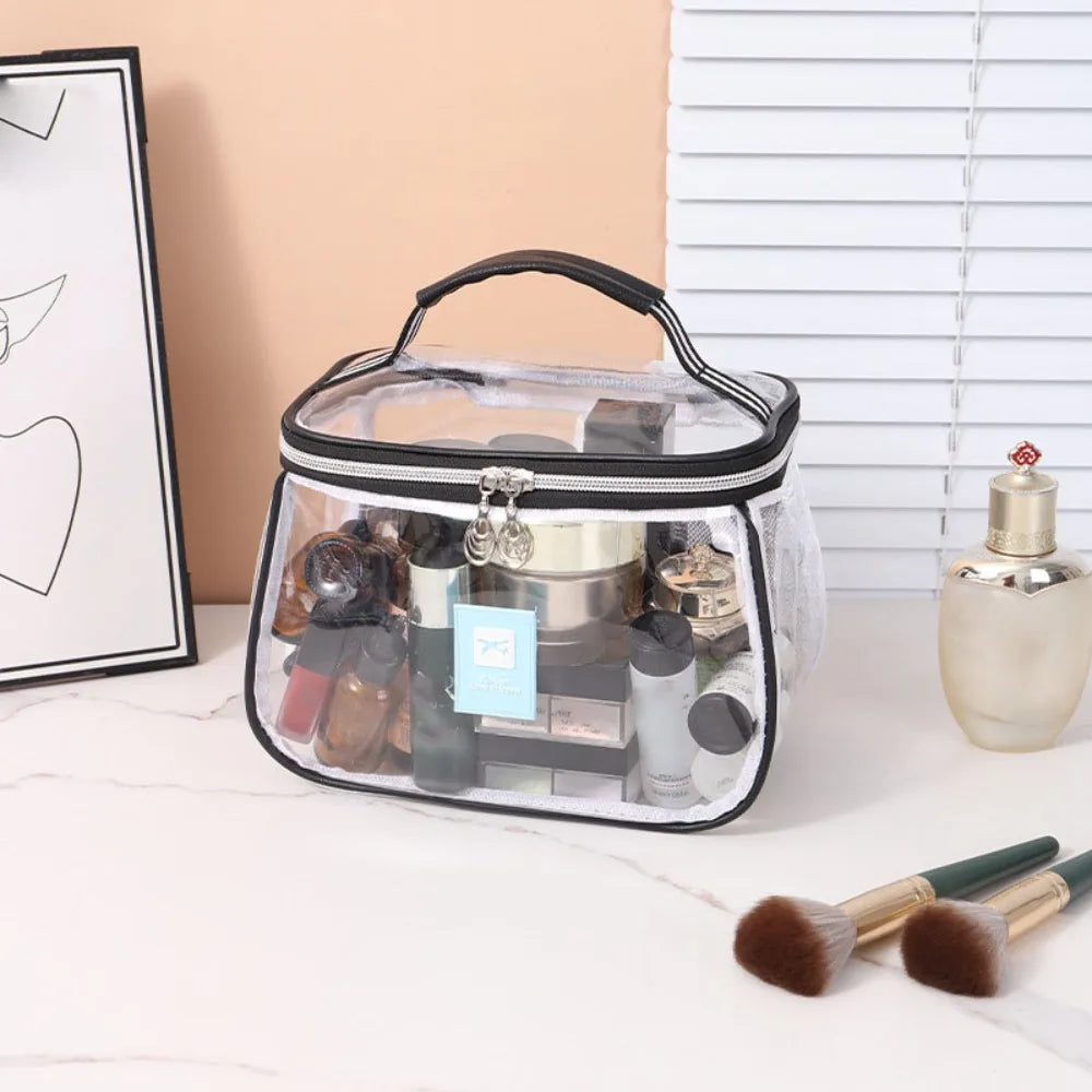 A clear cosmetic bag with a black zipper and handle filled with various makeup products on a white surface.