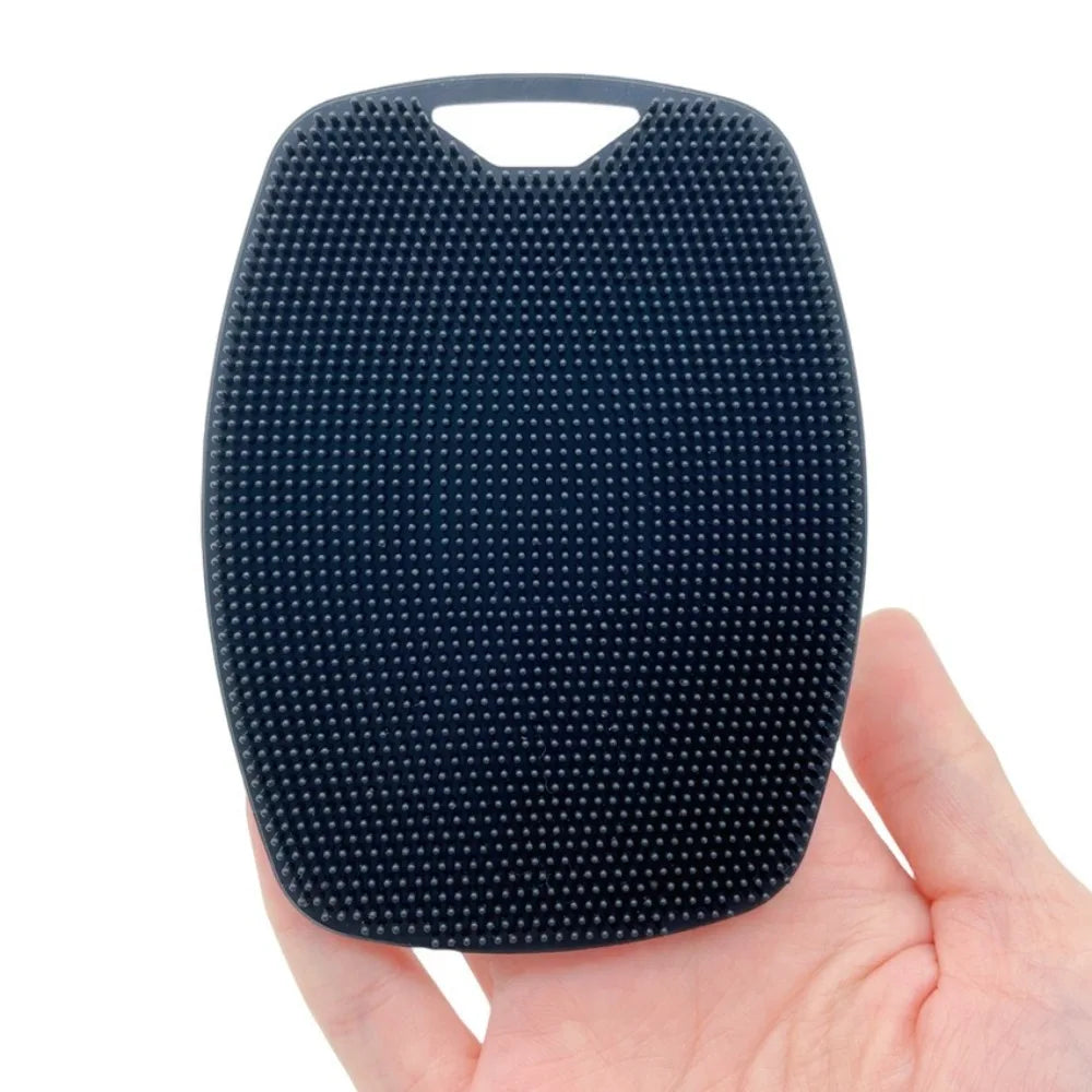 A hand is holding a dark blue silicone body brush with a handle, ready for shower or bath use.