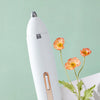 A white electric hair cutter with a rose-colored handle is shown against a light green background.