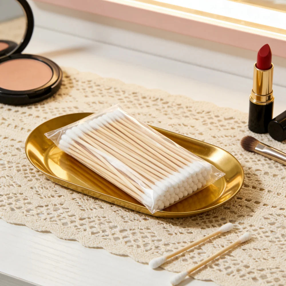 A tray of precision wooden cotton swabs with white tips rests on a beige textured cloth next to a gold plate.