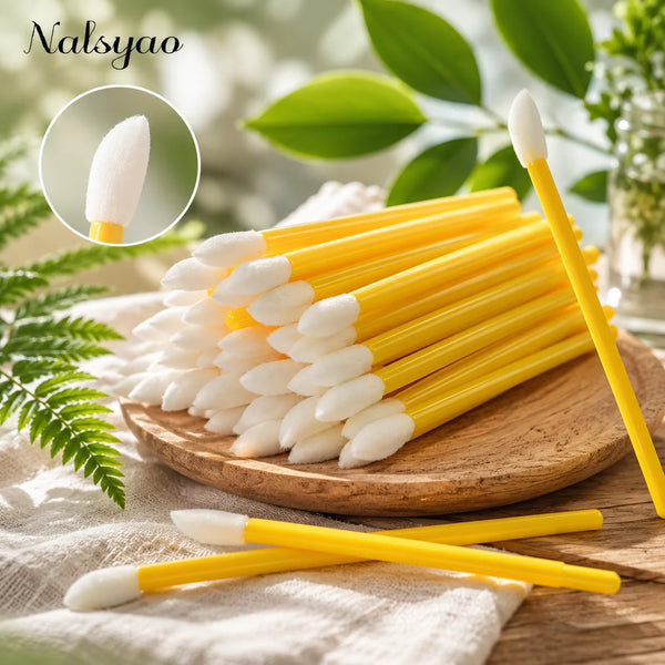A wooden board holds a large set of yellow and white disposable lip applicator brushes with a small white brush shown in deta