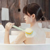 A woman is using a long-handle loofah back scrubber with a soft mesh sponge while bathing.