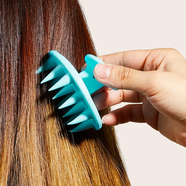 A hand is using a teal silicone brush to massage the scalp and hair of a person.