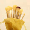 A set of professional makeup brushes in gold and yellow housed in a yellow fabric pouch.