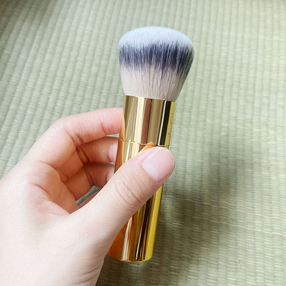 A hand holds a gold-handled bamboo airbrush foundation and bronzer brush with a silver-tipped bristles.