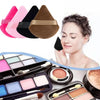 A woman applies a triangular velvet powder puff, surrounded by various colored powder products and brushes.