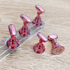 Un ensemble de supports à ongles magnétiques roses métalliques avec des boutons décoratifs, présentés dans un support en acry