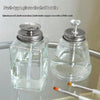 A clear push-type glass alcohol bottle dispenser with a silver pump top and a white stick inside.
