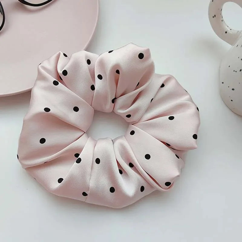 Scrunchies en satin à pois roses, noués en nœud froncé sur une surface blanche.