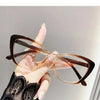 A hand is holding a pair of brown-framed cat eye reading glasses with clear lenses against a light gray background.