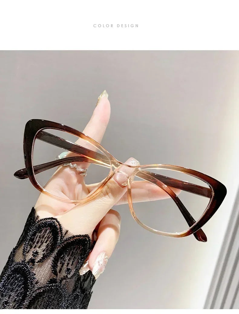 A hand is holding a pair of brown-framed cat eye reading glasses with clear lenses against a light gray background.
