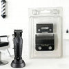 A black hair clipper replacement blade is shown next to its clear plastic packaging.