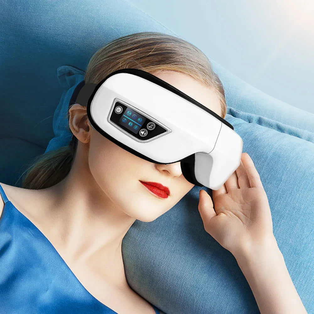 A woman is using a white portable Bluetooth eye massager on her face while lying down.