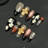 Un set de uñas postizas talladas a mano con diseño de pétalo de almendra y acentos florales dorados sobre fondo negro y nude.