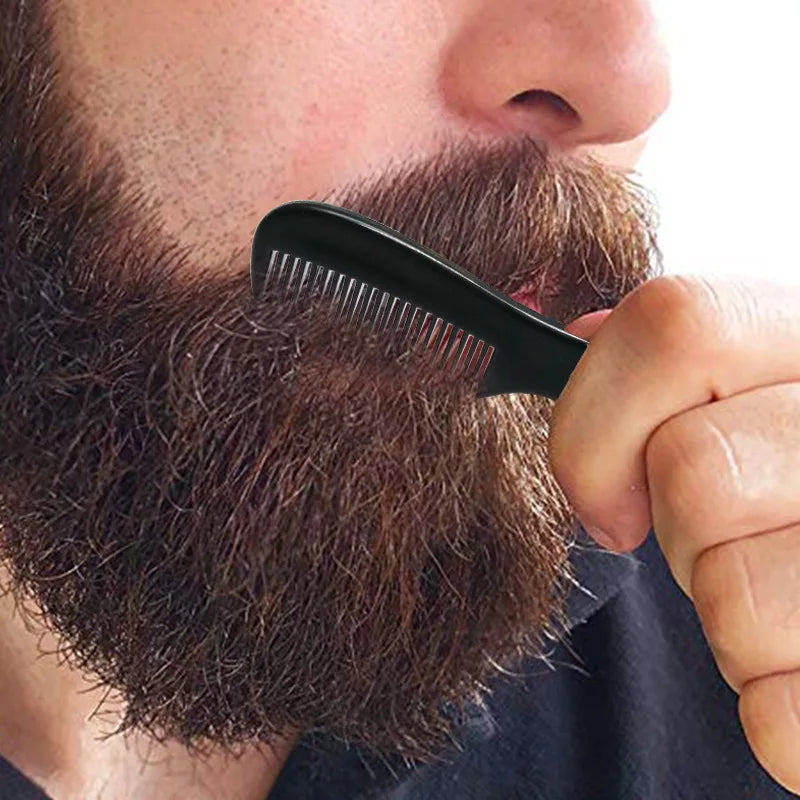 A hand holds a black portable mini pocket beard comb against a person's brown beard.