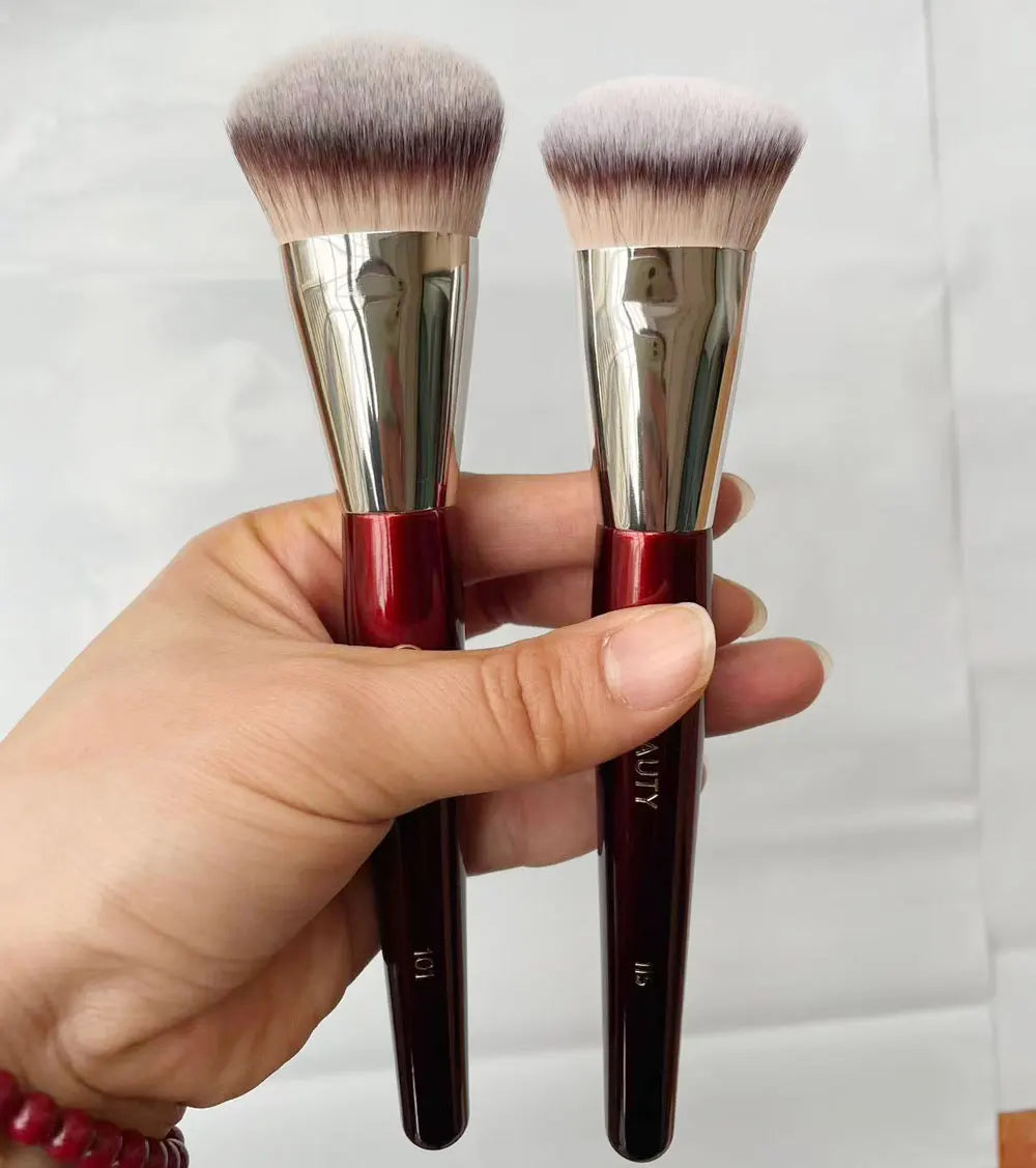 Une main tient deux pinceaux de maquillage pour fond de teint liquides inclinés avec des poils roses et violets.