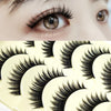A close-up of a pair of long, thick black false eyelashes on an eye, next to a palette of eyelash strips.