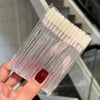 A hand holds a clear plastic kit of crystal lip brushes and lash spoolies.