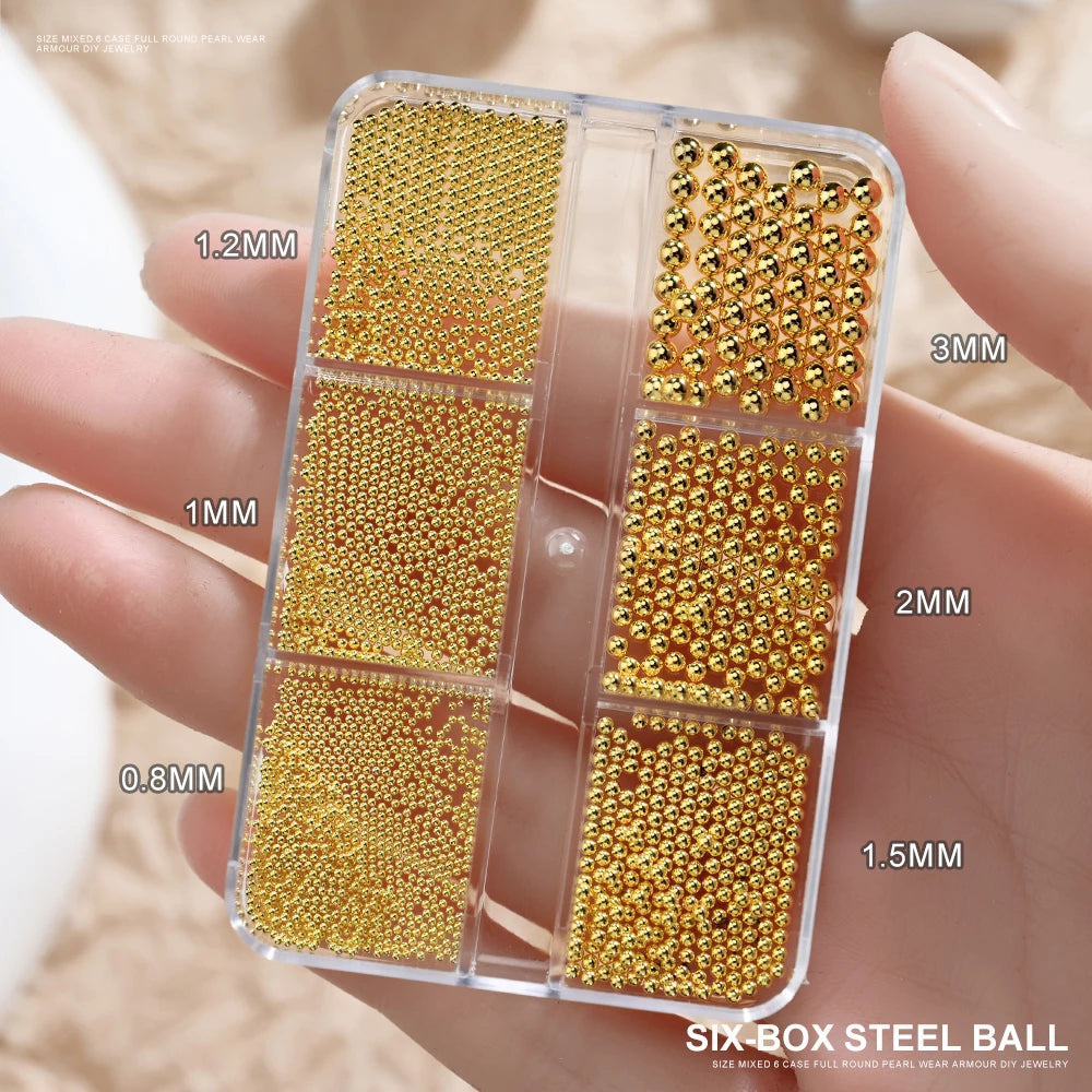 A clear box holds various sizes of gold mixed stainless steel beads for nail art decorations.