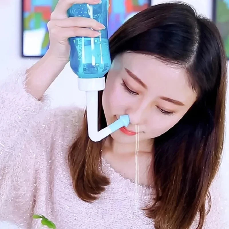 A woman is using a blue nasal irrigation bottle to irrigate her nose.