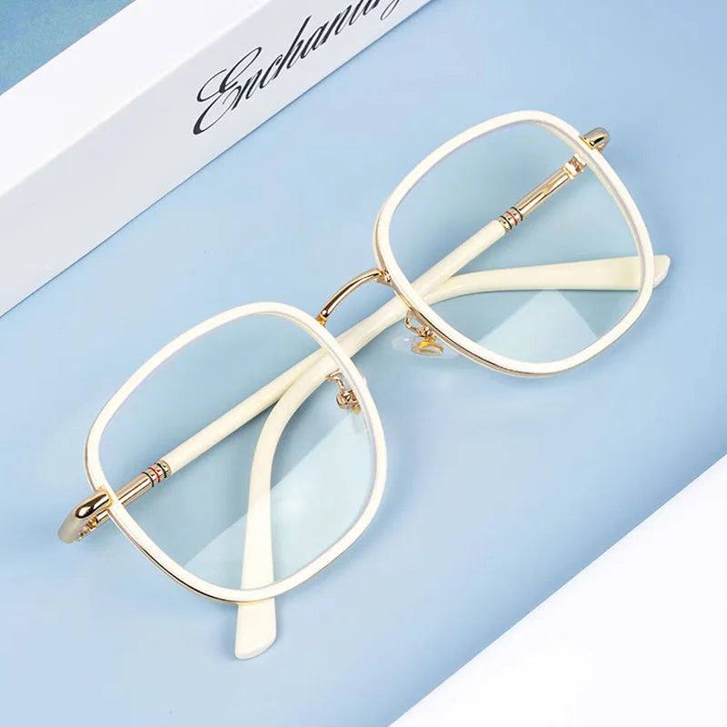 A pair of white-framed reading glasses with gold accents resting on a light blue surface.