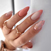 A hand displaying press-on false nails with a soft pink and nude gradient and gold accents.