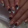 Nahaufnahme einer Hand, die lange, klebrige, falsche Nägel mit schwarz-weißem Design und goldenen Blumenakzenten zeigt.