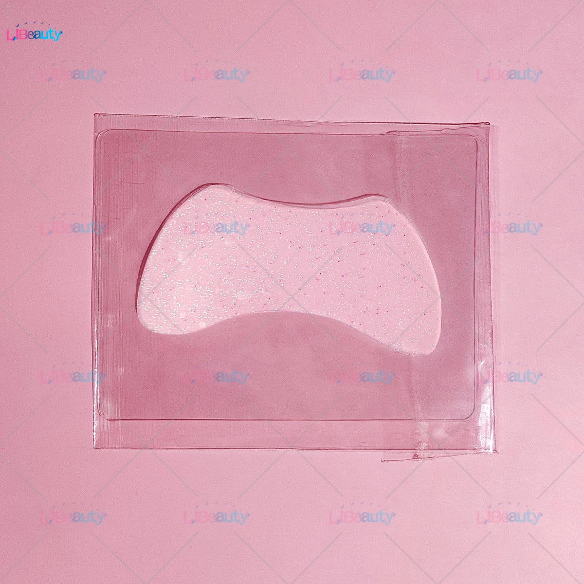 A clear silicone lash lift shield eye pad with a pink glittery cosmetic product inside.