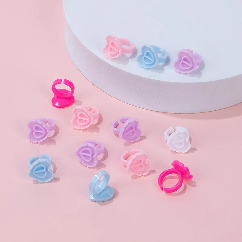 A collection of pink and blue disposable glue rings for eyelash extensions and nail art displayed on a white surface.