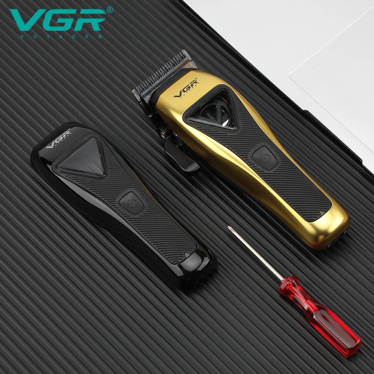A gold and black professional rotary hair clipper with a red cleaning tool shown on a dark surface.