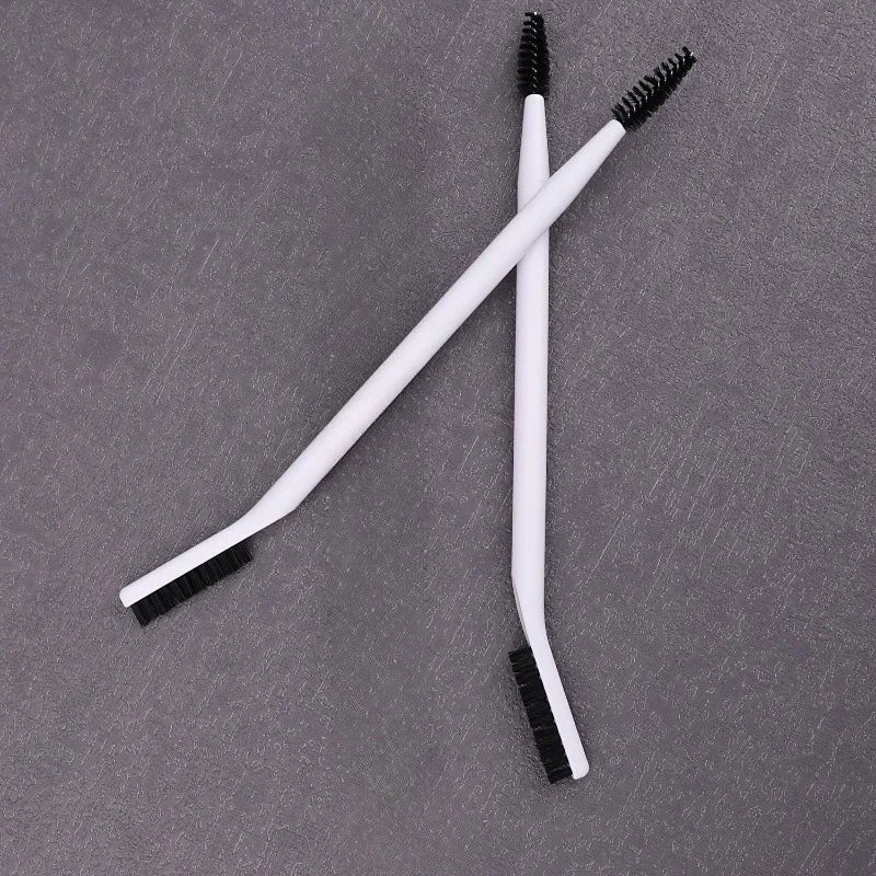 A pair of white dual-ended eyelash curlers and brow brushes are displayed on a gray surface.