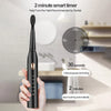 A hand holds a black ultrasonic electric toothbrush with various cleaning modes displayed on the body.
