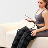 Eine Frau benutzt einen Air Wave Beinmassierer an ihren Beinen, während sie auf einem Sofa sitzt.