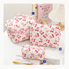 A pink quilted cotton makeup bag with a zipper closure is shown next to a book and a white lamp.