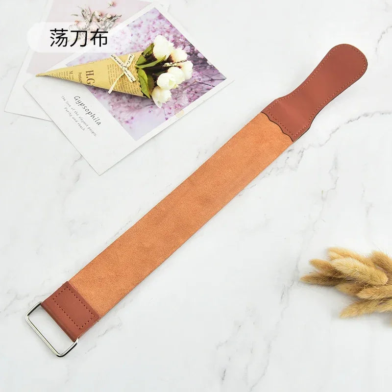 A brown leather sharpening strop with a wooden handle is displayed on a white marble surface next to a small plant card.