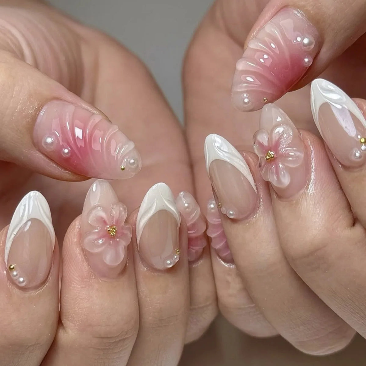 A close-up of hands displaying 24-piece almond press-on nails featuring delicate pink and white floral designs.